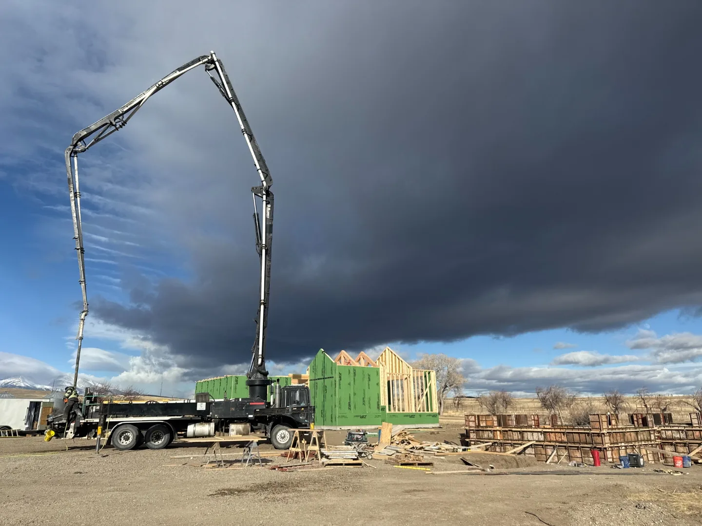 Concrete boom pump set up beside a framed home under storm clouds